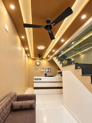 A reception area with a reception desk, a ceiling fan, a clock, and a staircase. - HOTEL ROYAL MANSION SOMNATH (Veraval)