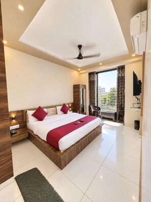 A modern hotel room with a large bed, a ceiling fan, a TV, and a balcony with a view. - HOTEL ROYAL MANSION SOMNATH (Veraval)