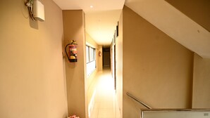 A hotel hallway with a fire extinguisher, a small flower arrangement, and a staircase. - HOTEL ROYAL MANSION SOMNATH (Veraval)