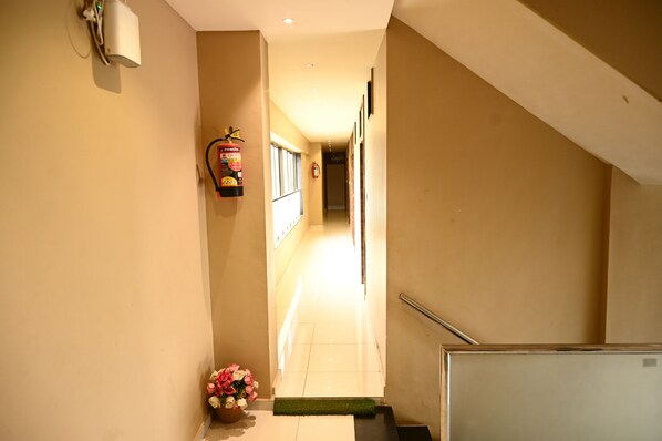 A hotel hallway with a fire extinguisher, a handrail, and a small flower arrangement.
