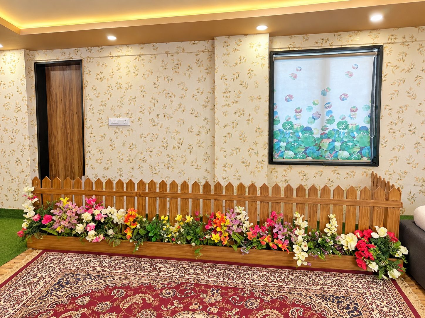 A room with a patterned wall, a wooden fence with flowers, a patterned rug, and a window with a floral view.