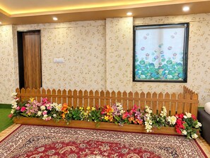 A room with a patterned wall, a wooden fence with flowers, a patterned rug, and a window with a floral view.