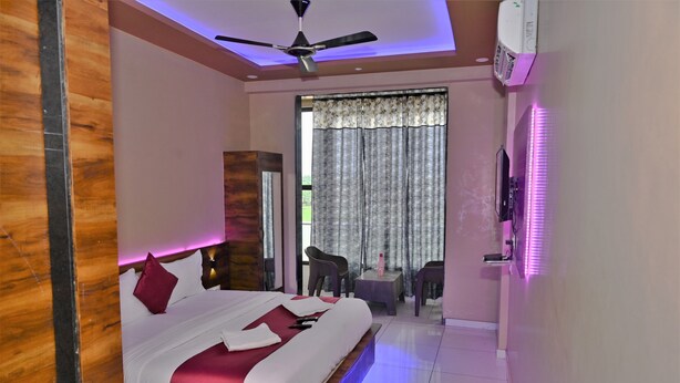 A hotel room with a bed, a ceiling fan, a TV, a small table, and a chair. - HOTEL ROYAL MANSION SOMNATH (Veraval)