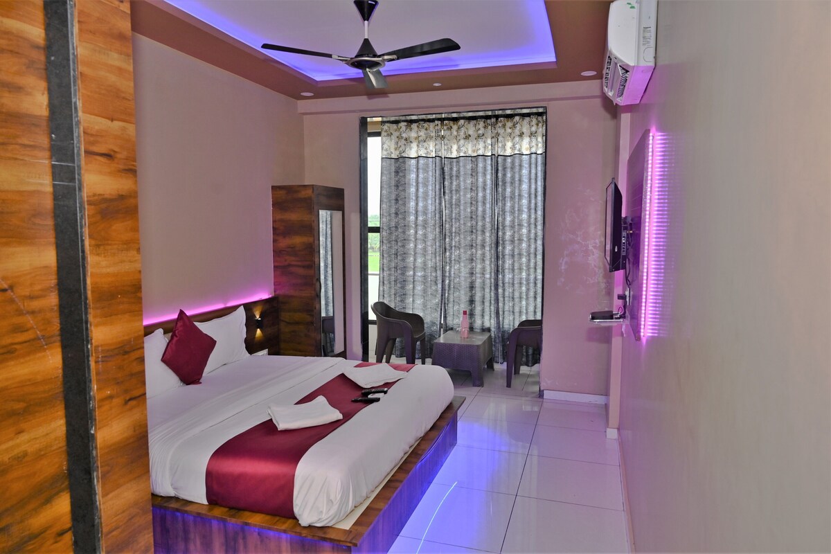 A hotel room with a bed, a ceiling fan, a TV, a small table, and a chair.