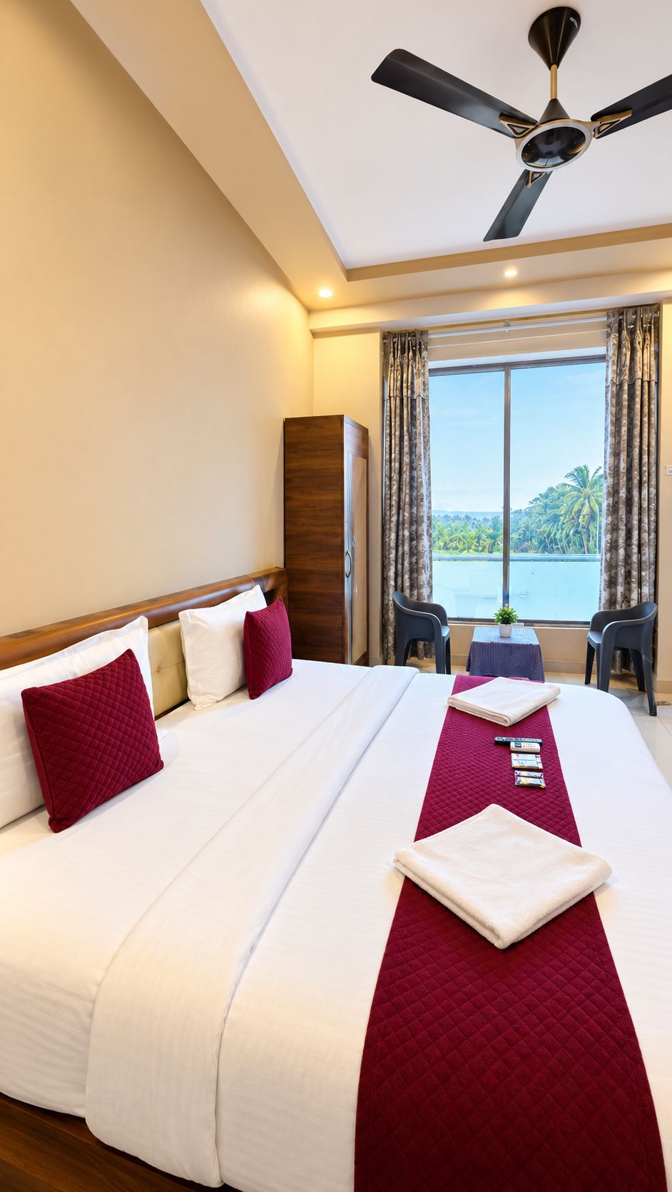 Une chambre d’hôtel avec un lit, un ventilateur de plafond, une vue sur l’extérieur et une petite table avec des chaises.
