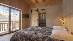 Ein Schlafzimmer mit einem großen Bett, einer Glastür zum Balkon, einem an der Wand befestigten Fernseher und einer Holzbalkendecke.