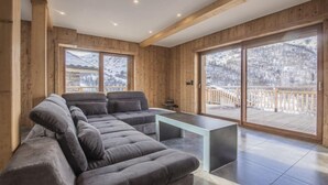 Ein modernes Wohnzimmer mit einem Ecksofa, einem Glastisch und großen Schiebeglasüren zum Deck.