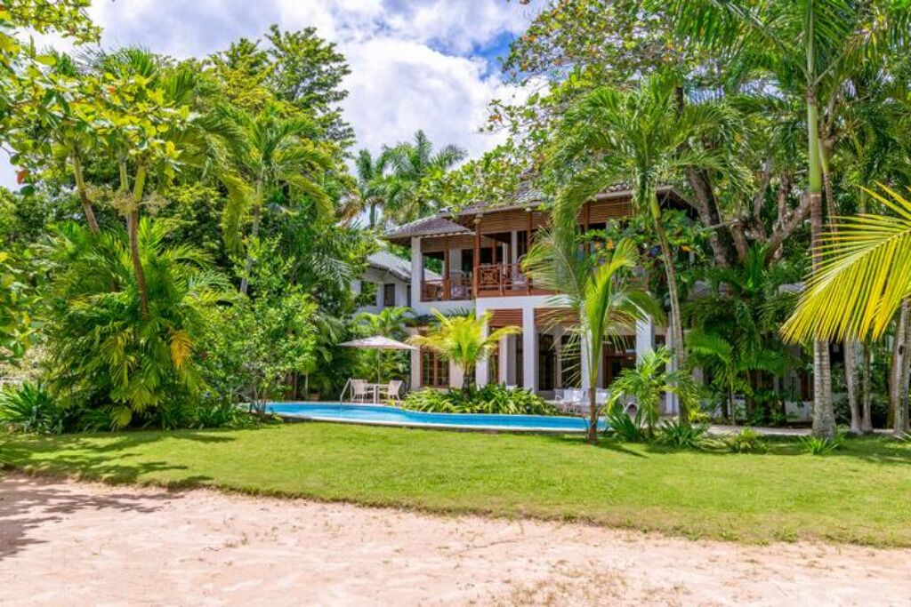 A tropical resort with a pool, lush greenery, and a two-story building.