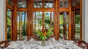 Mesa de comedor dispuesta para seis personas, con mantel blanco, sillas de madera y un florero en el centro.