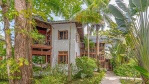 A two-story building with a white exterior and wooden balconies, surrounded by lush tropical vegetation.