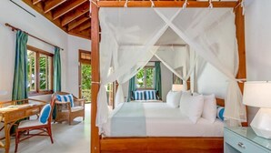 A four-poster bed with a canopy, a wooden desk with chairs, and a nightstand with a lamp.