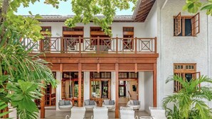 A two-story building with a balcony, outdoor seating area with white lounge chairs, and tropical plants.