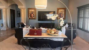 Ett rymligt vardagsrum med modern design, inrett med en stor platt-TV, ett matbord med en röd låda och en dekorativ vas med blommor.