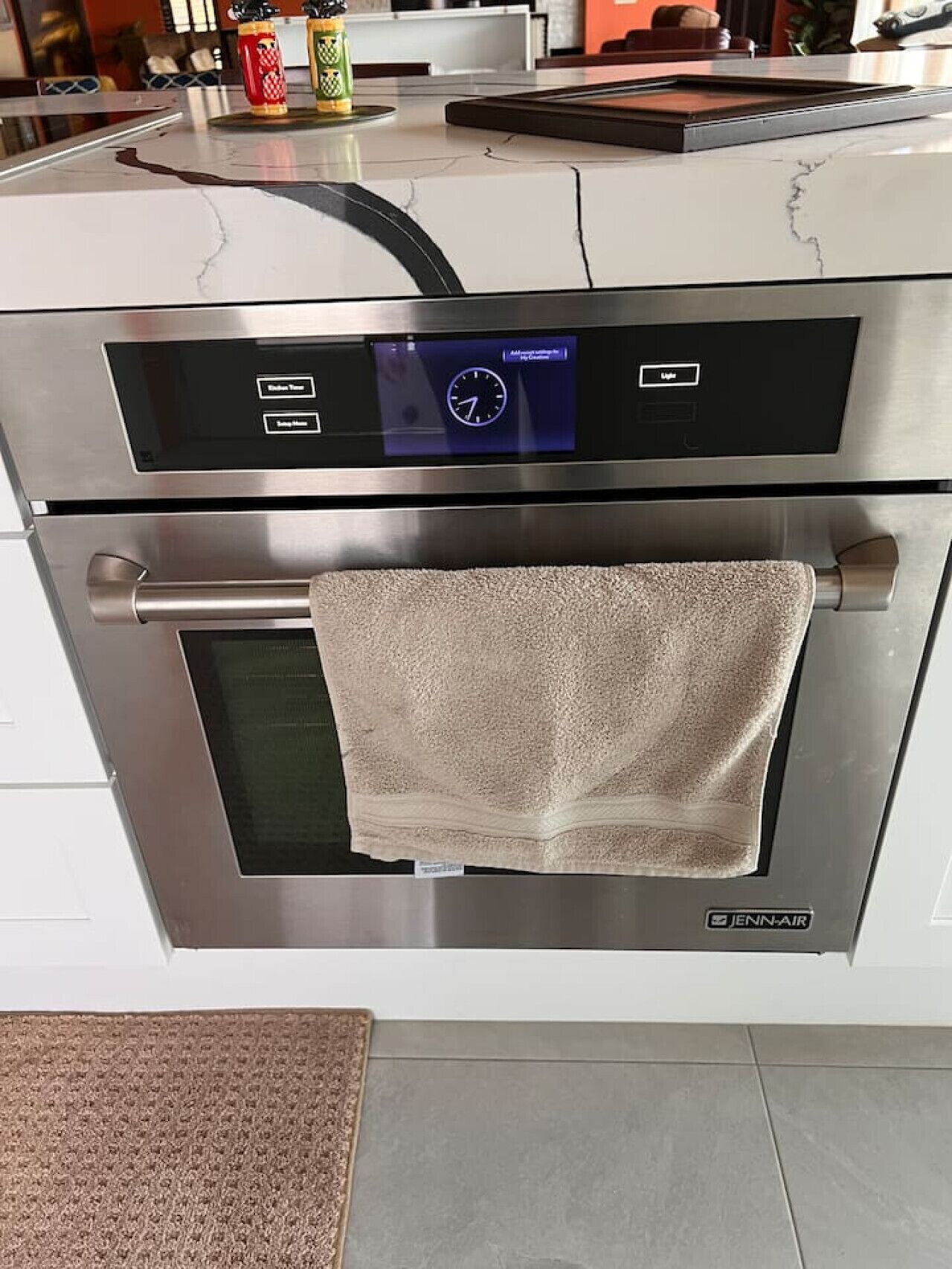 A kitchen with a stainless steel range hood, a digital clock, and a towel hanging on the oven handle.