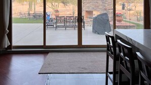A room with a large sliding glass door leading to an outdoor patio with a stone wall, seating, and a covered grill area.