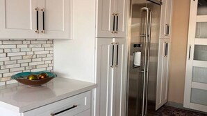 A modern kitchen with white cabinetry, a stainless steel refrigerator, and a marble backsplash.