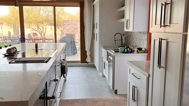 A modern kitchen with white cabinets, a large island, and a view of the outdoors.