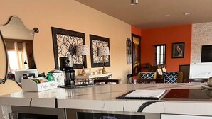 A modern kitchen with a built-in oven, a coffee bar, and a dining area with a sofa and table.