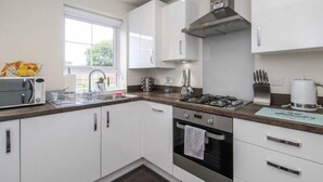 A modern kitchen with white cabinets, a gas stove, an oven, and a window providing natural light. - EV Charger, Airport Access, City Centre (Speke)