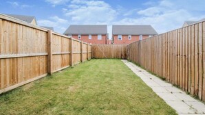 A fenced backyard with a grassy lawn and a paved walkway. - EV Charger, Airport Access, City Centre (Speke)