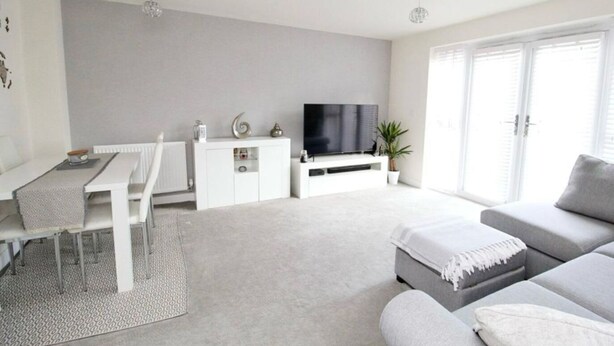 A modern living room with a grey sofa, a dining table with chairs, a TV on a white cabinet, and a large window with blinds. - EV Charger, Airport Access, City Centre (Speke)