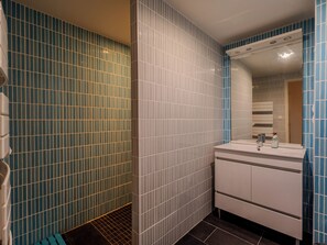 Un baño con paredes cubiertas de azulejos azules y blancos, un lavabo blanco con espejo, y una zona de ducha con piso de diseño de cuadrícula.