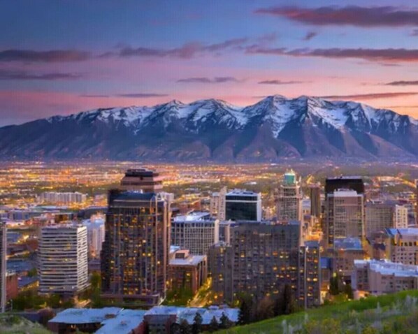 A cityscape with high-rise buildings and a mountain range in the background. - The Beehive Loft Gym Parking Garage (Salt Lake City)