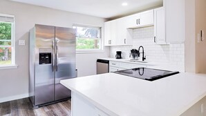 A modern kitchen with white cabinetry, a stainless steel refrigerator, a built-in oven, and a window providing natural light.
