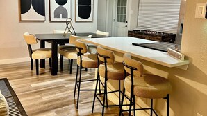 A modern kitchen with a bar area, wooden flooring, and abstract wall art.