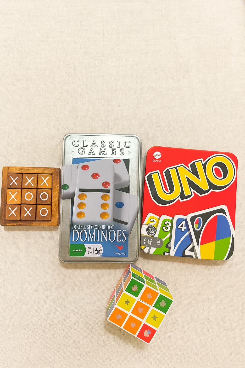 Four board games: Double Six Color Dot Dominos, UNO, a wooden game board, and a Rubik's Cube.