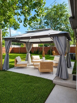 A covered patio area with outdoor furniture, a pergola, and a grassy lawn.