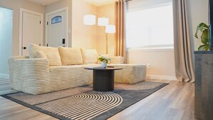 A living room with a sofa, a coffee table, a lamp, and a window with curtains.