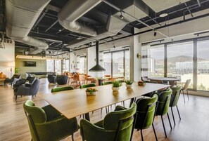 Un espacio de oficina moderno con una mesa larga y sillas verdes, ventanas amplias y vista a la ciudad.