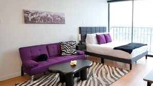 A modern bedroom with a bed, a purple sofa, a black coffee table, and a zebra-patterned rug.