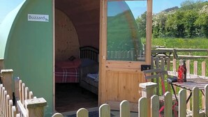 Een kleine, groene, koepelvormige tent met een open houten deur, waarbinnen een bed te zien is.