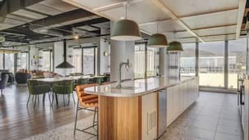Uma cozinha moderna com uma ilha central, banquetas de bar, iluminação pendente e grandes janelas com vista para a cidade.