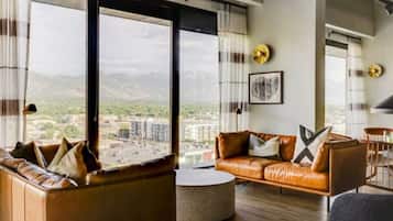 Uma sala de estar moderna com sofás de couro, uma mesa de centro redonda e grandes janelas com vista para a cidade.
