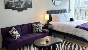 Ein modernes Hotelzimmer mit einem Bett, einem violetten Sofa, einem kleinen Tisch und einem zebra-gestreiften Teppich.