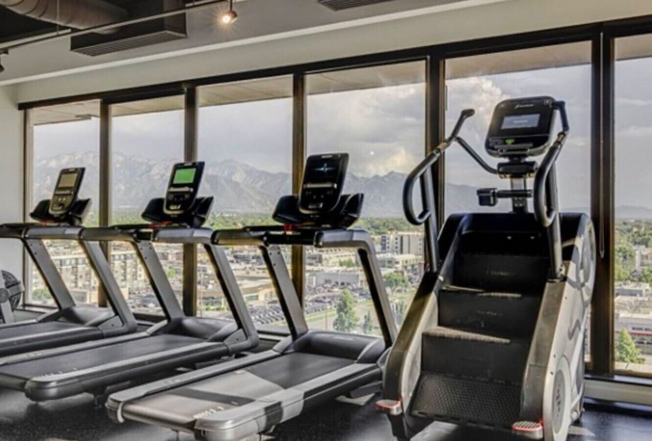 Een sportschool met loopbanden en een stair climber, grote ramen met uitzicht op de stad.