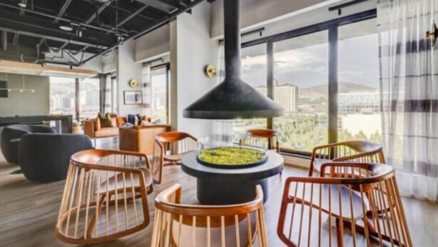 Un salón moderno con una chimenea central, asientos y ventanas amplias que ofrecen vista a la ciudad.