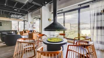 Een moderne lounge met een centraal haardelement, zitplaatsen en grote ramen met uitzicht op de stad.