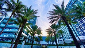 Un hotel moderno con diversi piani, palme e cielo sereno.