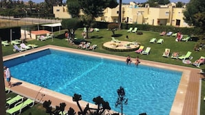 En swimmingpool med liggestole og en grøn område med træer.