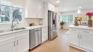 A modern kitchen with white cabinetry, stainless steel appliances, and a large window providing natural light. - Spacious 5BR Retreat-Sleeps 10+ (El Cajon)
