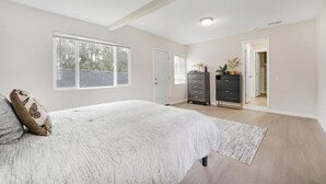A bedroom with a large bed, a dresser, and a wardrobe. There is a window providing natural light and a door leading to another room. - Spacious 5BR Retreat-Sleeps 10+ (El Cajon)