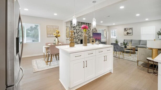 A modern kitchen with white cabinetry, pendant lighting, and a dining area with a gray sofa and a coffee table. - Spacious 5BR Retreat-Sleeps 10+ (El Cajon)