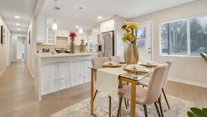 A modern kitchen with a dining area, featuring a glass table, bar stools, and a vase with flowers. - Spacious 5BR Retreat-Sleeps 10+ (El Cajon)