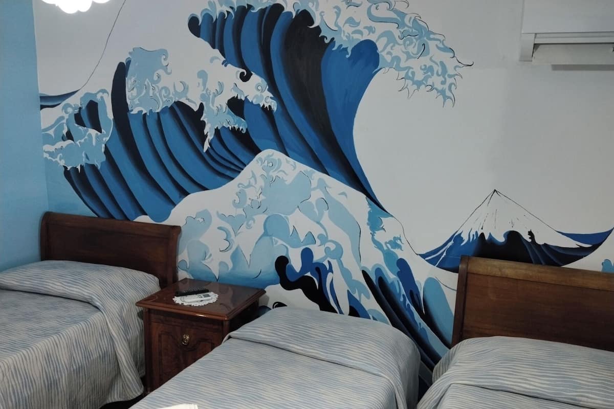 A hotel room with two beds, a nightstand, and a large wave painting on the wall.