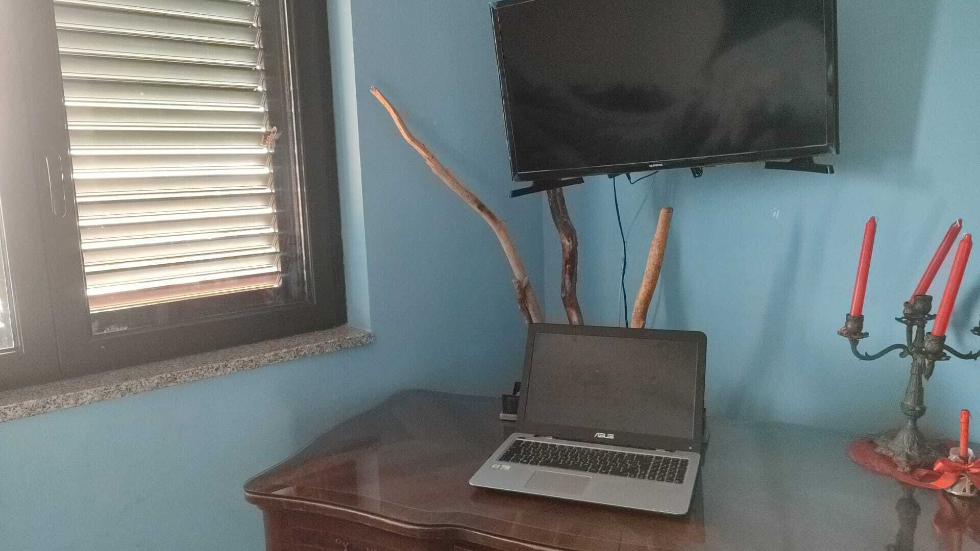 A laptop on a wooden desk, a TV on the wall, and a candelabra with candles.
