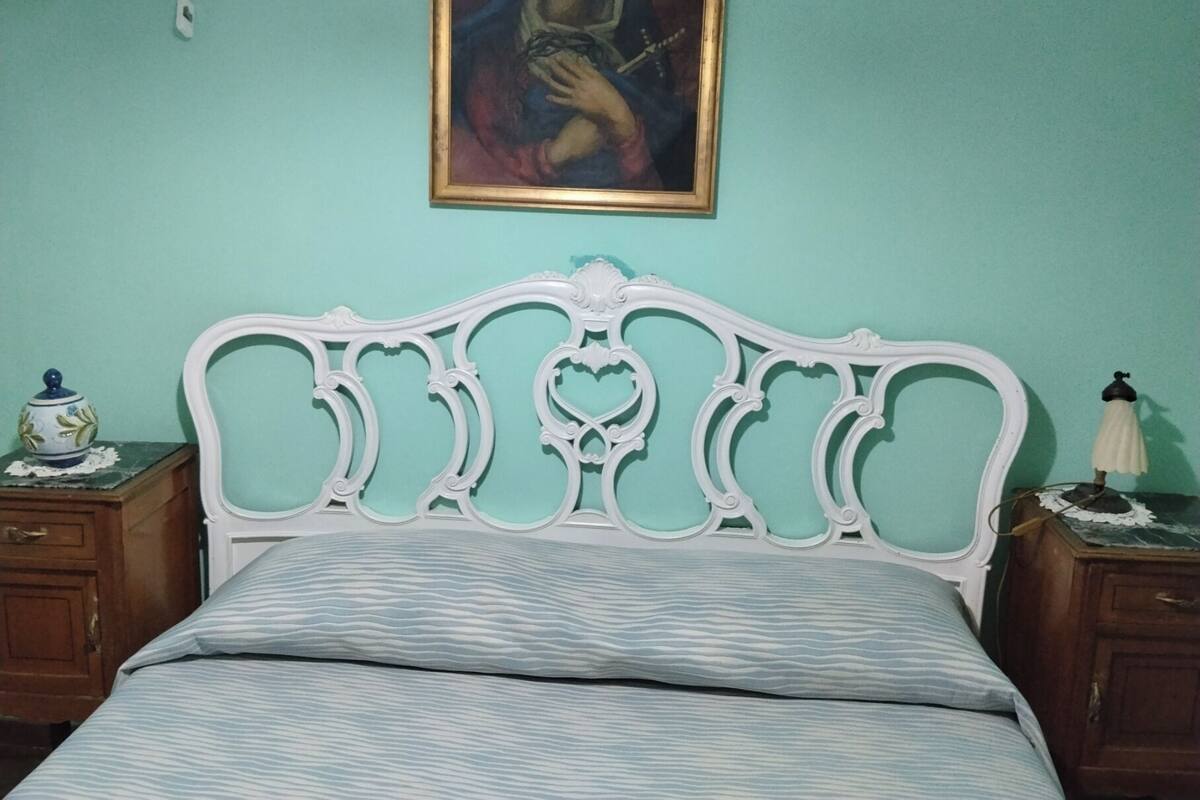 A room with a bed, a nightstand, a lamp, and a painting on the wall.